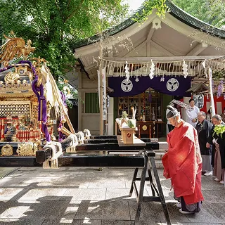例大祭。金色の神輿が台に据えられ、赤い装束の神職が前で厳かに拝礼している様子