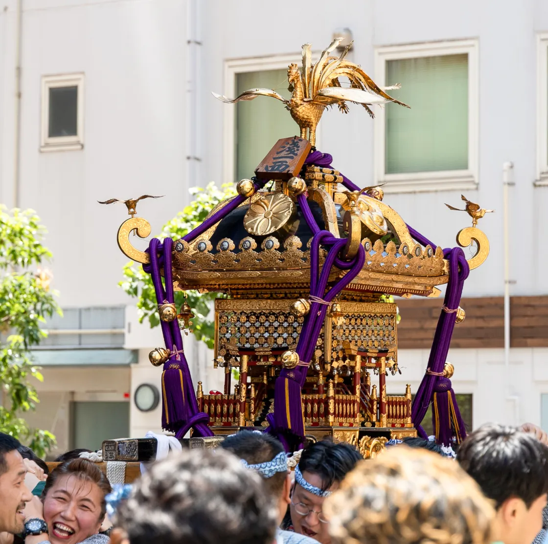金色の鳳凰が載った豪華な神輿を、多くの担ぎ手が担いで進む様子